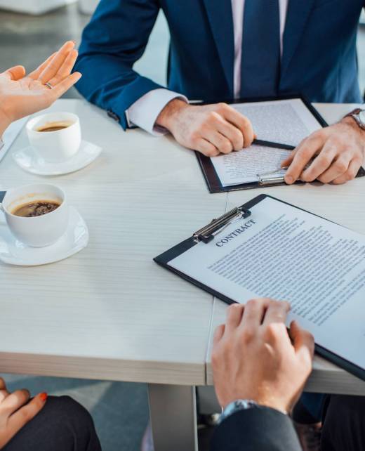 cropped view of professional business partners signing contract on meeting in office with coffee