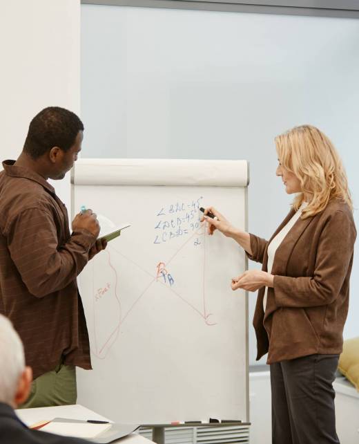 Mature woman with blond hair making notes on flipchart and discussing it together with teacher during presentation at class